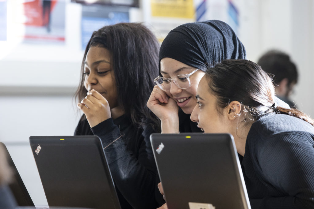 Three students sat around laptops talking