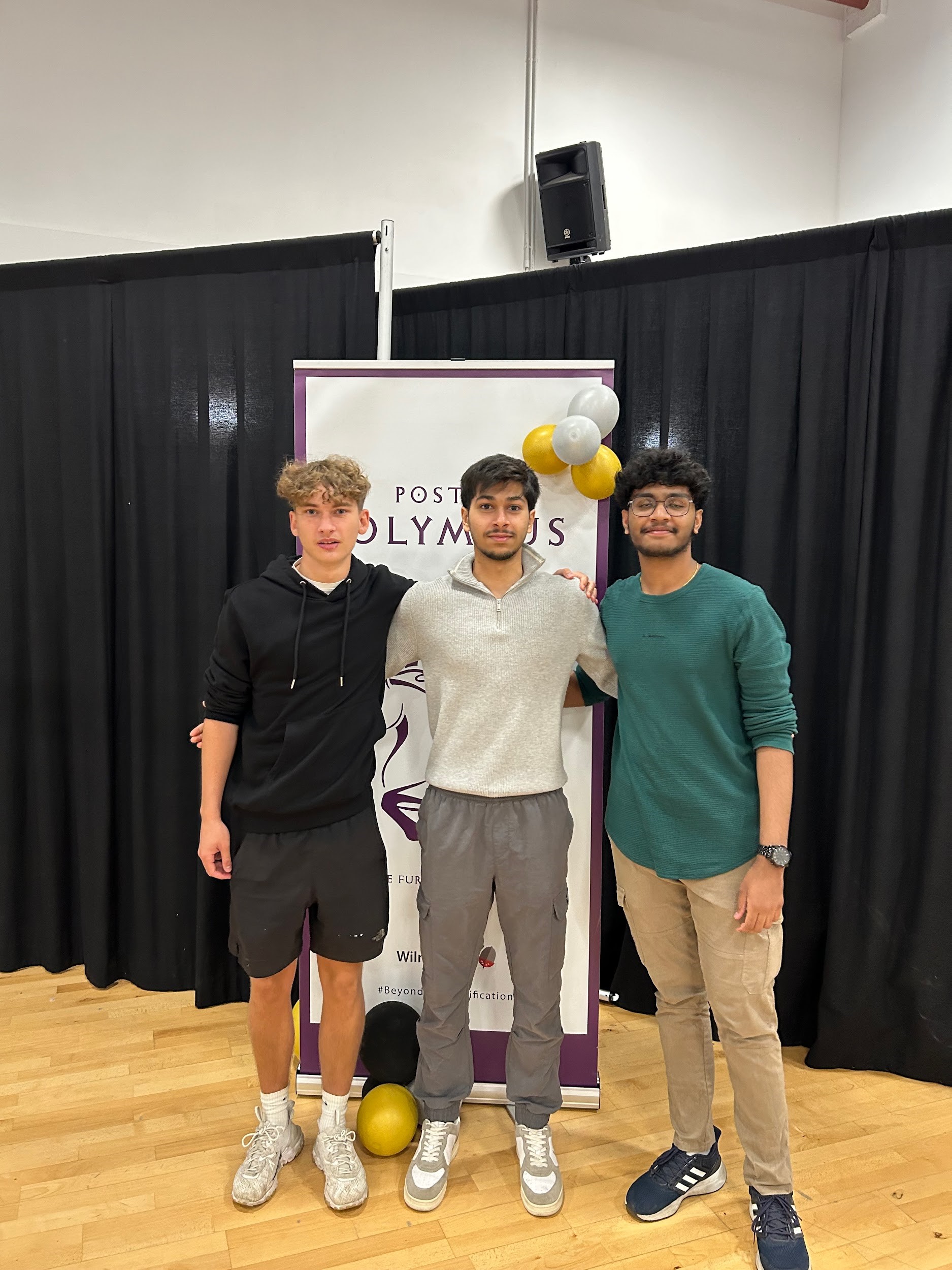 3 male students standing in front of an IB banner