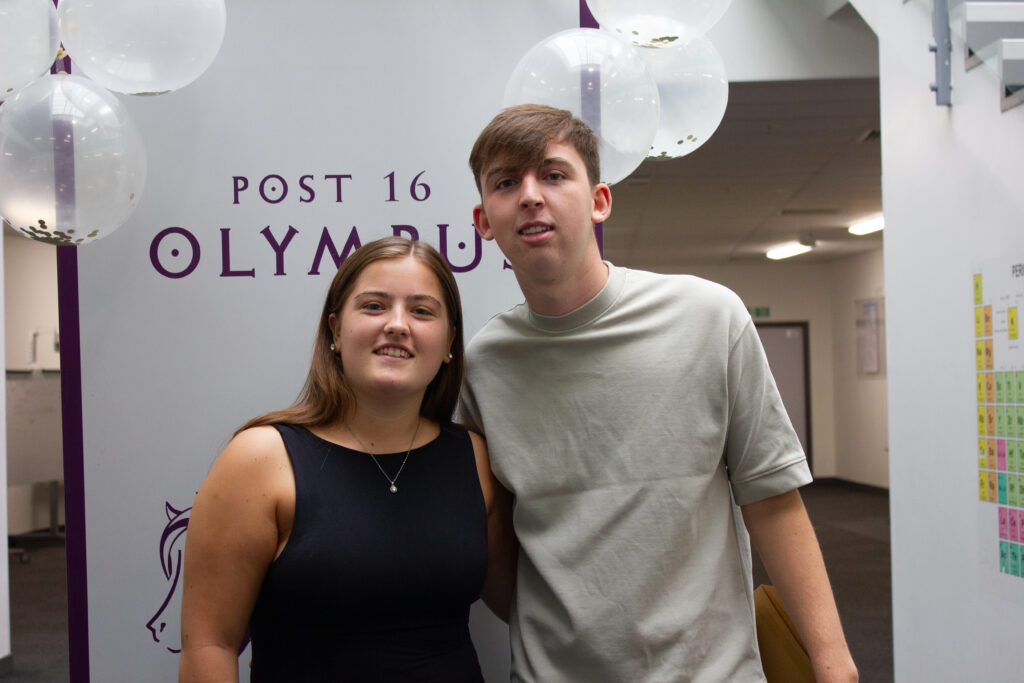 Two Post-16 students, one male and one female, are pictured smiling for the camera, whilst holding their A-Level results in their hands.