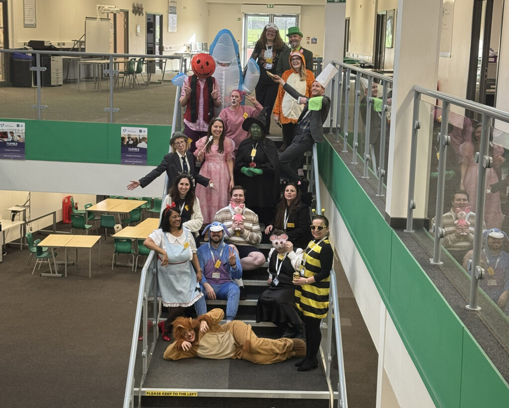 A large group of adults wearing diverse, colorful costumes poses together on a staircase inside a building.